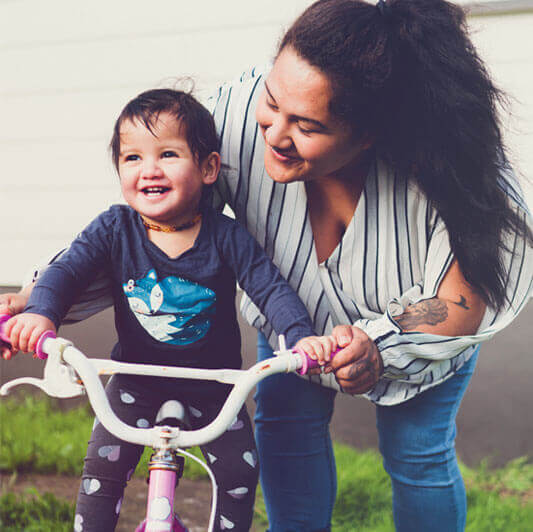 Mother steering a toddler on a pink bike - mobile